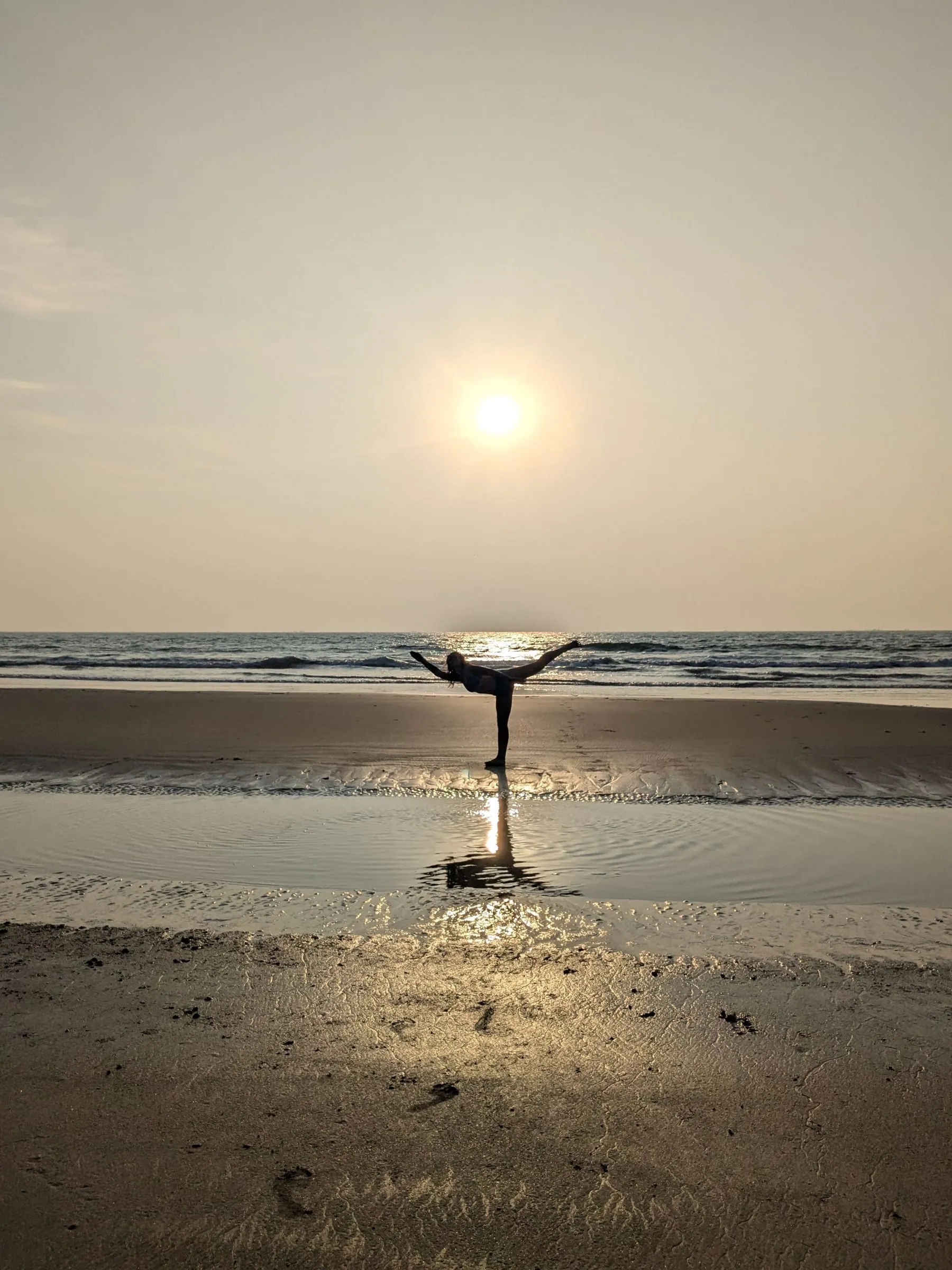 Laura en équilibre sur une jambe sur une plage, le soleil bas sur la mer