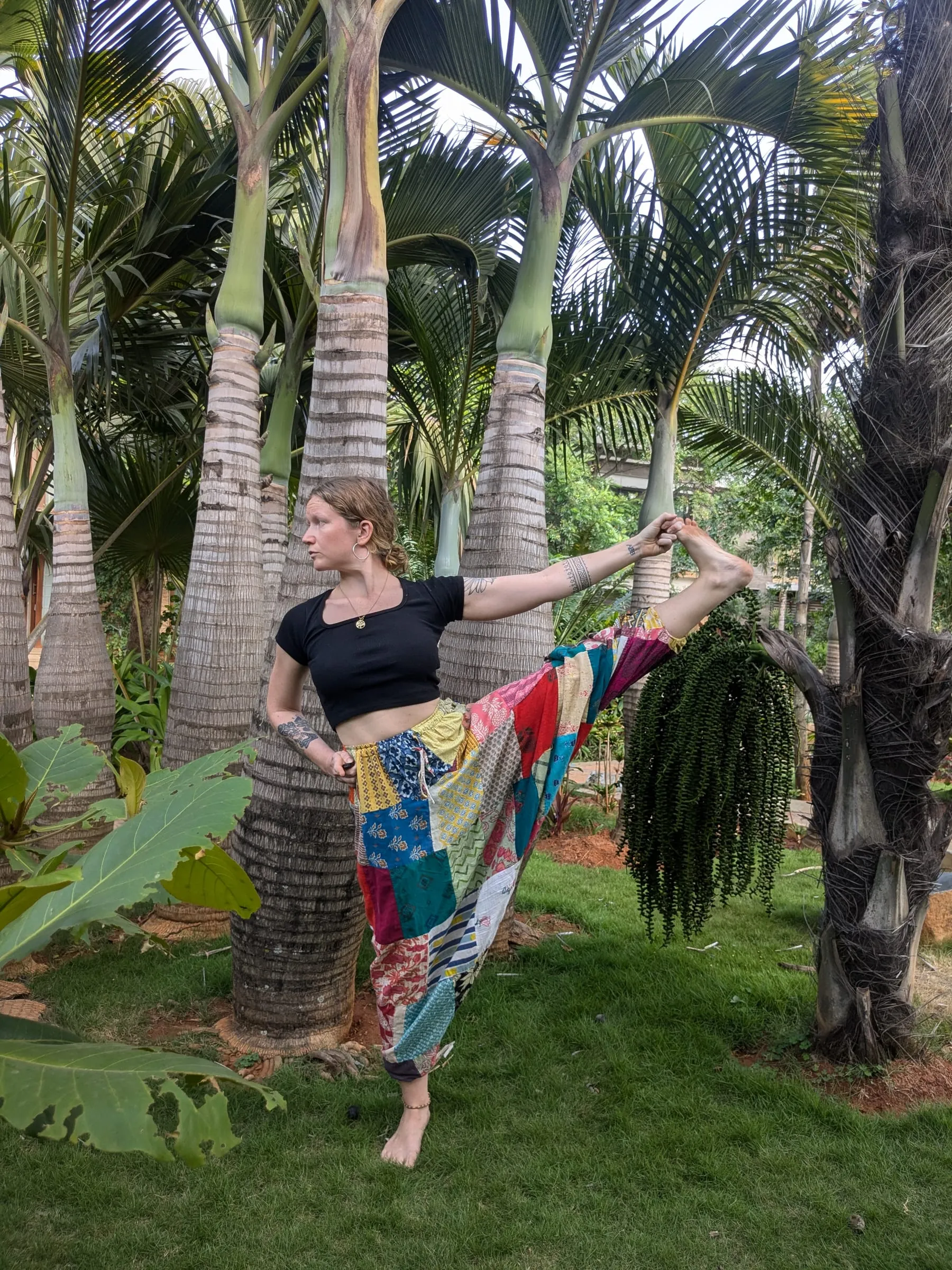 Laura en équilibre sur une jambe dans un jardin de palmiers, tenant sur le côté le gros orteil de sa jambe levée
