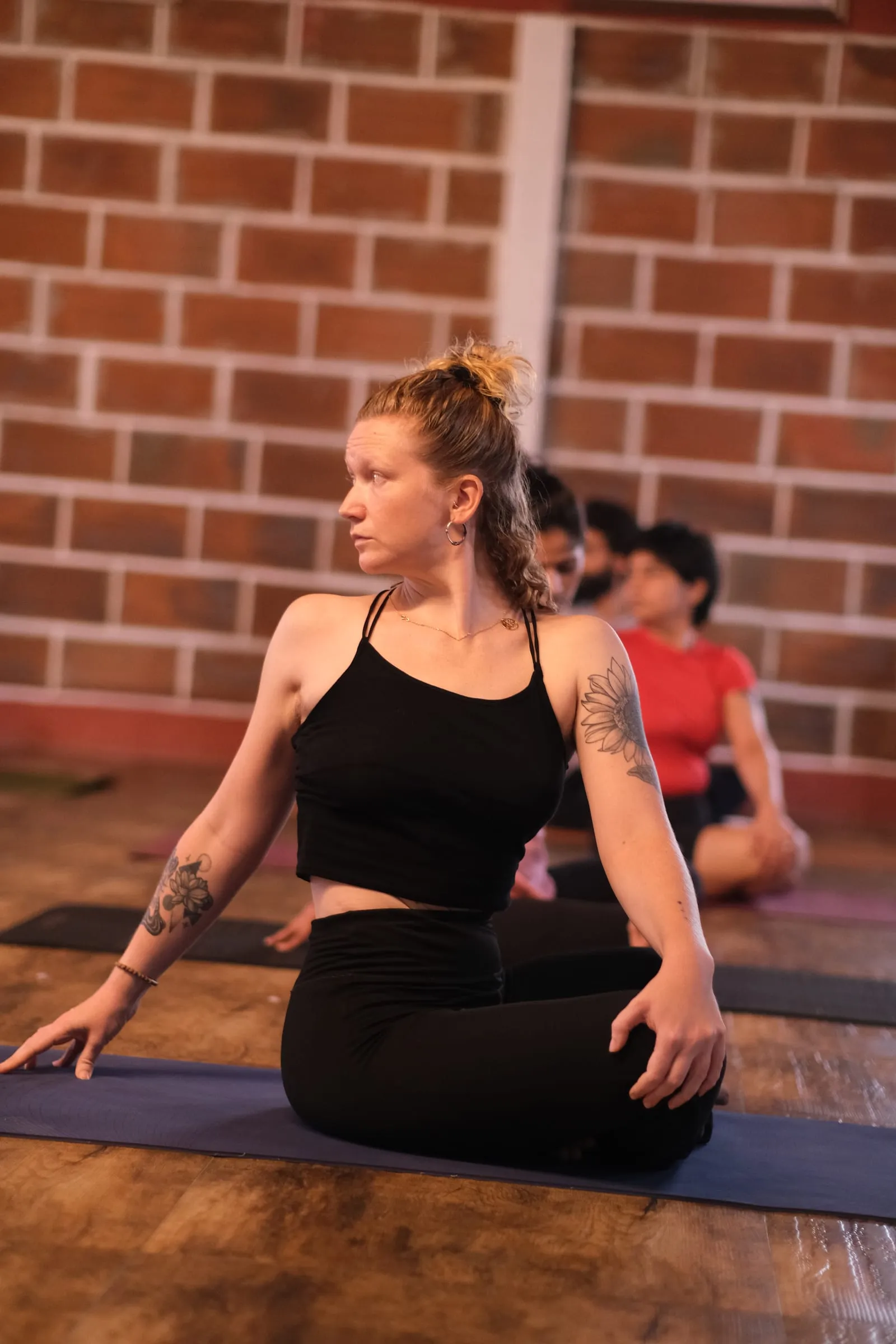 Laura en torsion assise sur son tapis, dans une salle de pratique