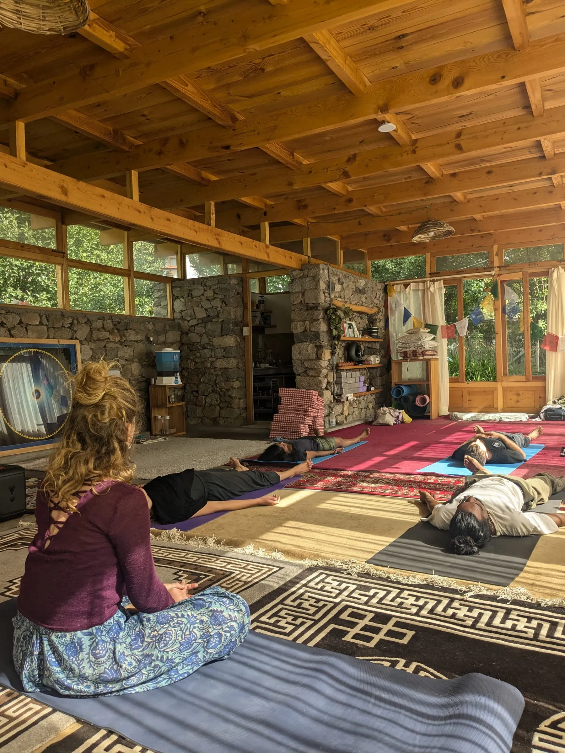 Laura assise face à un groupe allongé en relaxation, dans une salle en bois